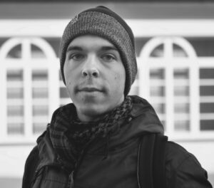 Monochrome close-up portrait of a man in a beanie and scarf looking directly at the camera